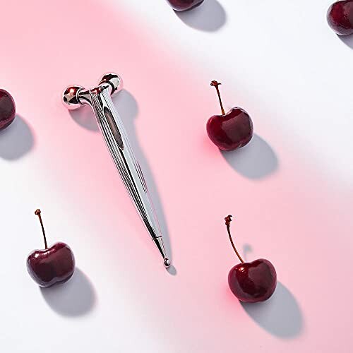 Metal facial massager with cherries on a white background.